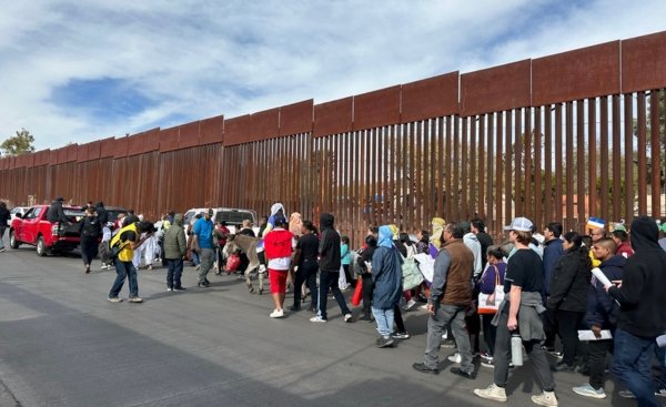 group of people walking along the United States border wall to Mexico
