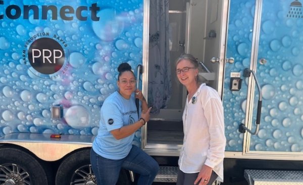 Sister Kristin with a woman standing in front of the portable shower trailer