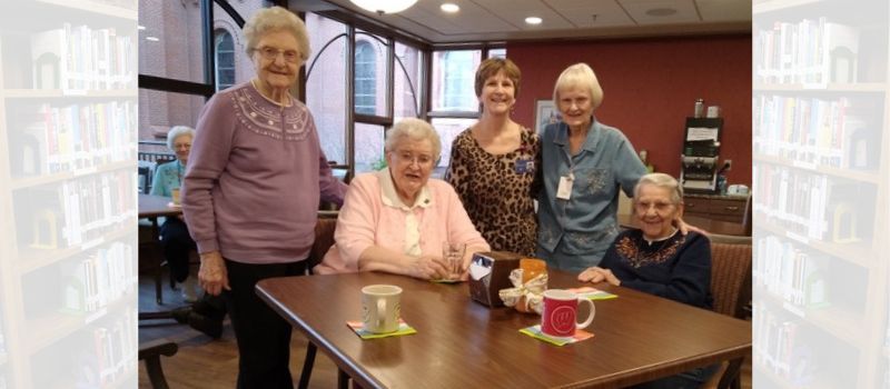 five women sitting around table in front of two coffee cups