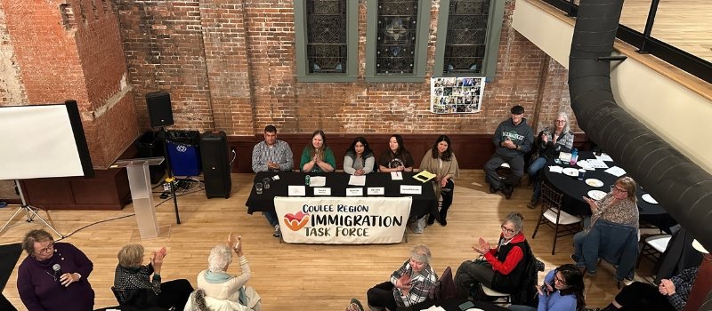 five people present at table placed in front of a crowd; people are clapping