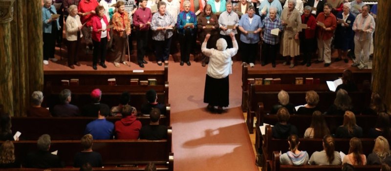 Sister Malinda Gerke stands in front of a choir directing their performance