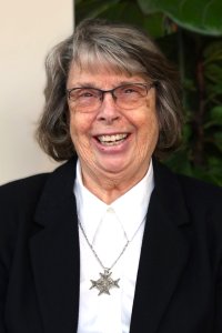 woman-with-glasses-graying-hair-black-suit-coat-white-button-up-shirt-and-silver-medal