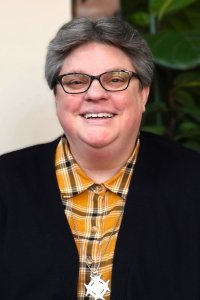 woman-with-glasses-short-gray-hair-black-sweater-black-and-yellow-plaid-shirt-and-silver-medal