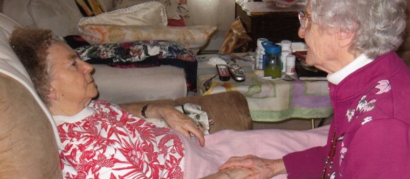 sister marcella sits bedside holding hands with a woman in hospice care